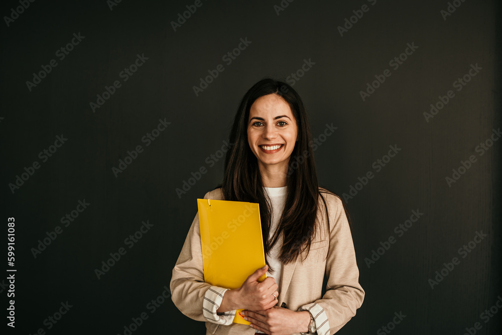 Portrait of a smiling businesswoman holding files and standing against the black background. Studio shot Portrait of a smiling businesswoman holding files and standing against the black background. Studio shot