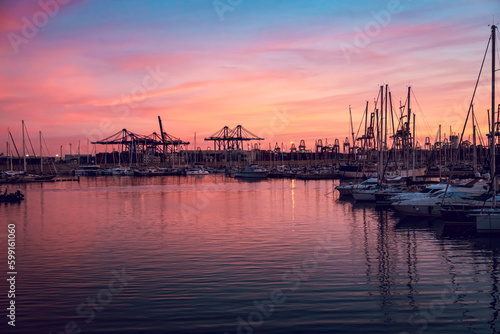 Yachts with reflection in the sea water of the port of Valencia. Port cranes on the horizon. Warm evening in Spain.