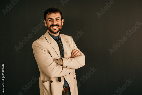 Portrait of a smiling businessman with arms crossed standing in a studio background.