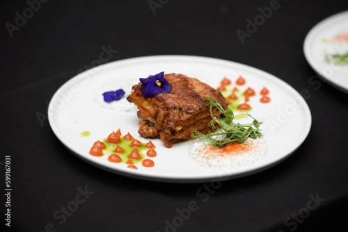 the chef in the restaurant preparing traditional greek moussaka in white plate on black tablecloth background