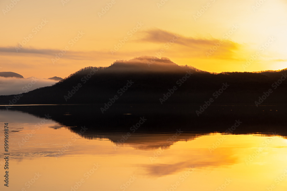 夜明けの湖の対岸の山のシルエット。
