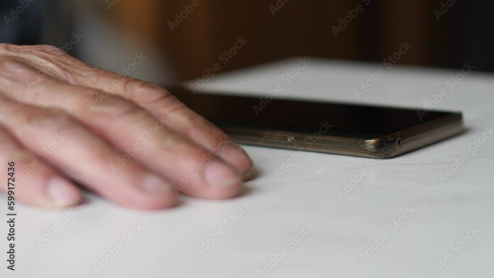 the hand of the old man close-up next to the phone lies on the table. selective focus. concept pensioner waiting for phone call, call parents, loneliness and despair concept the hand of the old man close-up next to the phone lies on the table. selective focus. concept pensioner waiting for phone call, call parents, loneliness and despair concept