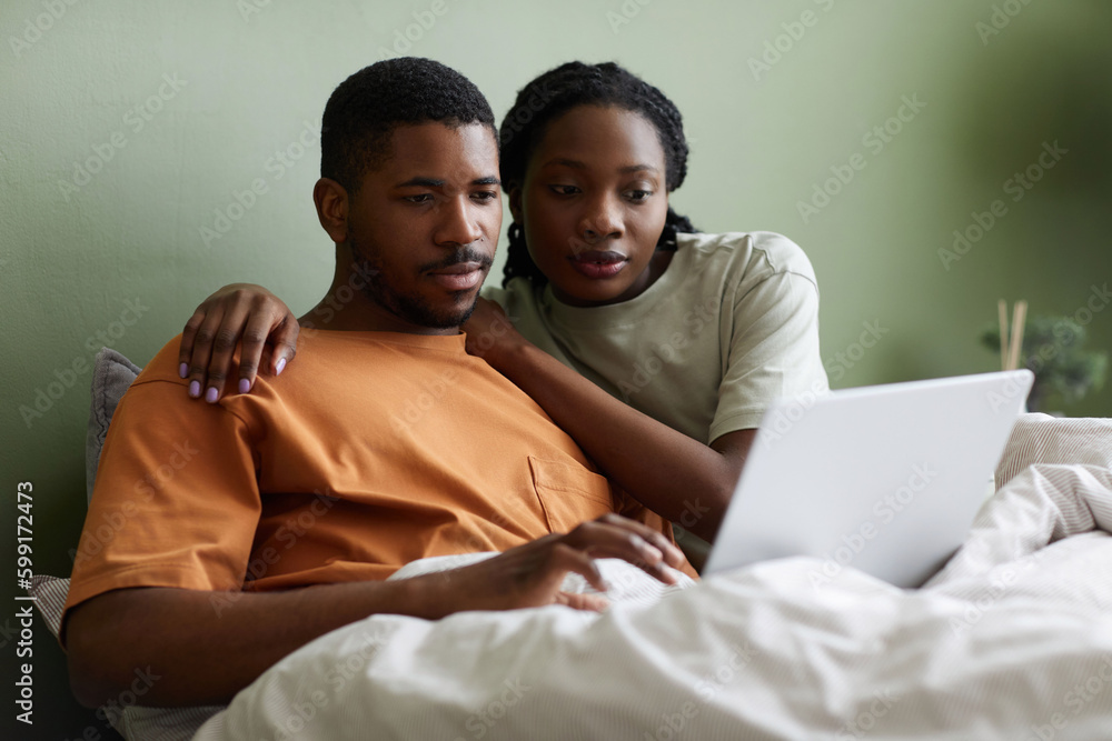African American young couple watching movie on laptop while resting in bed in bedroom African American young couple watching movie on laptop while resting in bed in bedroom