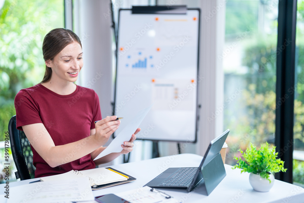 Young successful employee business woman in red shirt hold paper account documents work stand at workplace white desk with laptop pc computer at light modern office indoors achievement career concept Young successful employee business woman in red shirt hold paper account documents work stand at workplace white desk with laptop pc computer at light modern office indoors achievement career concept