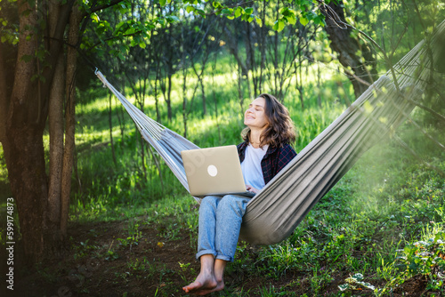 Obraz na płótnie Young cheerful dreamy woman sitting with laptop in hammock in summer garden, countryside lifestyle relaxing in nature w salonie