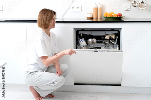 Busy housewife putting dirty plates in dishwasher machine in the kitchen. Household and exhausting cleaning day concept