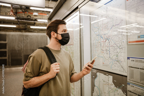 Young man using mobile phone and examining map while standing in subway photo