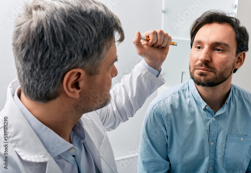 Foto Neurologist doctor examining male patient, checking basic reflexes of human by shining flashlight into his eyes