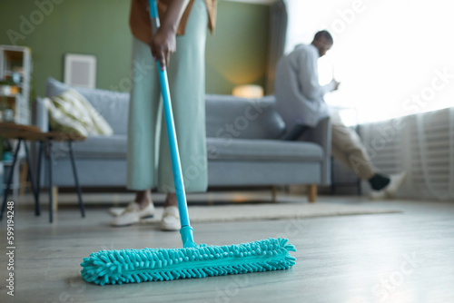 Photos Close-up of housewife wiping floor with mop during housework in the living room