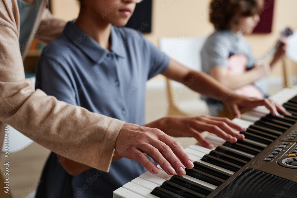Obraz premium Close-up of schoolgirl learning to play piano together with teacher during musical lesson in class