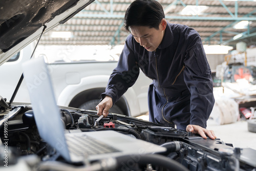 Car mechanic maintenance and auto service shop concept. Male car mechanic repair, fix car engine in auto repair shop. Technician inspecting quality parts of battery, electronic in garage workshop
