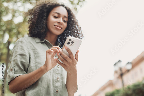 Young beautiful woman using smartphone in a city. Smiling student girl texting on mobile phone outdoor. Modern lifestyle, connection, casual business concept © kite_rin