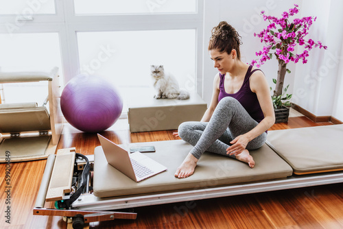 latin adult woman doing pilates exercises workout on reformer bed at home in Mexico, hispanic people in Latin America