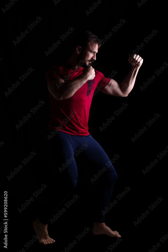 hombre creando una pose de artes marciales con malla azul y camiseta deportiva roja. Fotografía de estudio. Aislado sobre fondo negro. Espacio para texto