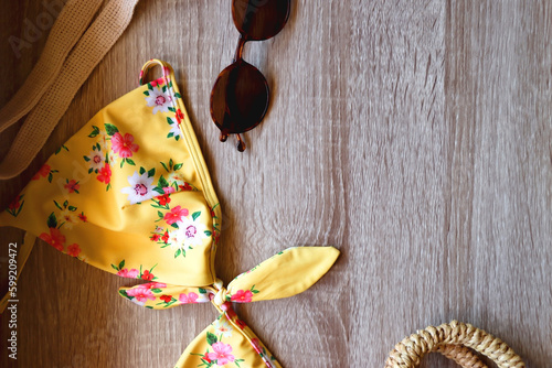 Floral yellow bikini, wicker bag, retro sunglasses, seashell, bag with peaches and cut watermelon on wooden background. Top view, copy space.