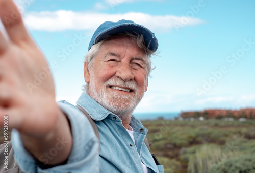 Portrait of happy senior bearded man outdoors in trekking day looking at camera. Elderly grandfather smiling enjoying healthy lifestyle and nature.