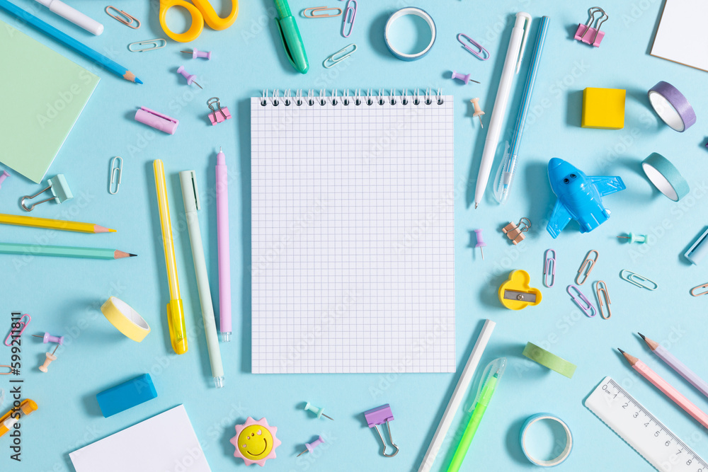 Back to school concept. Flat lay top view of scattered stationery notepad pens pencils paper clips airplane sticky tape note paper isolated on pastel blue background Back to school concept. Flat lay top view of scattered stationery notepad pens pencils paper clips airplane sticky tape note paper isolated on pastel blue background