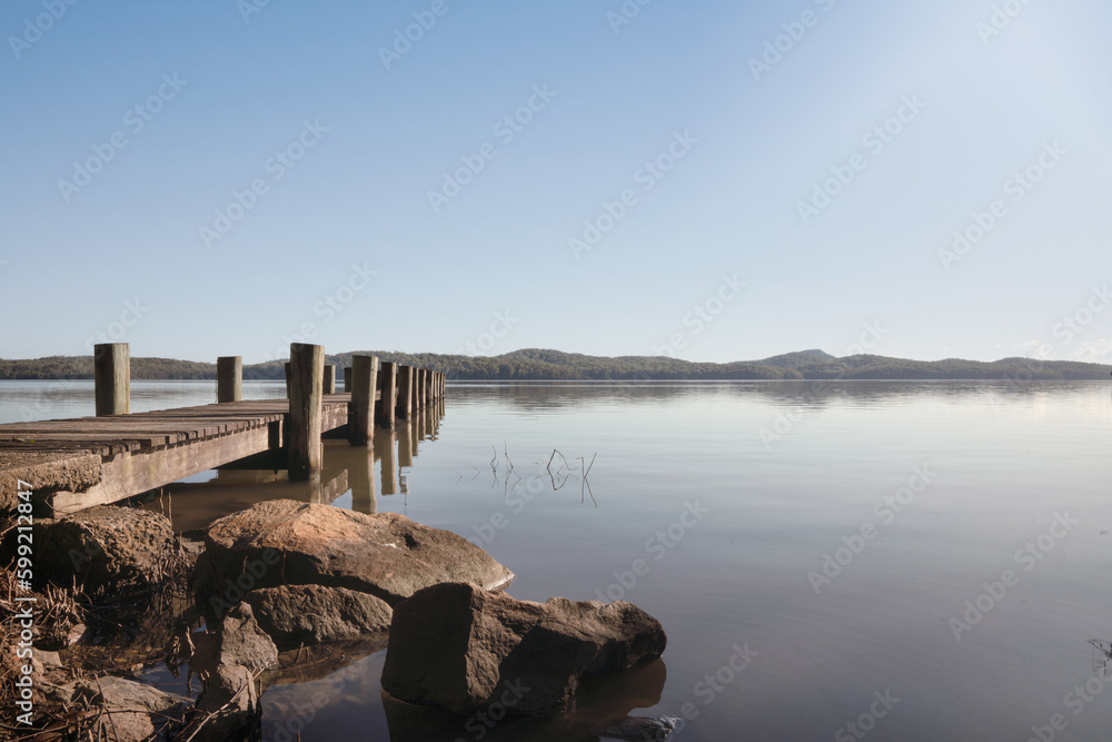 A bridge on a calm lake creates a reflection in the peaceful water. The tranquil atmosphere and surrounding vegetation add to the natural beauty of the scene. A bridge on a calm lake creates a reflection in the peaceful water. The tranquil atmosphere and surrounding vegetation add to the natural beauty of the scene.
