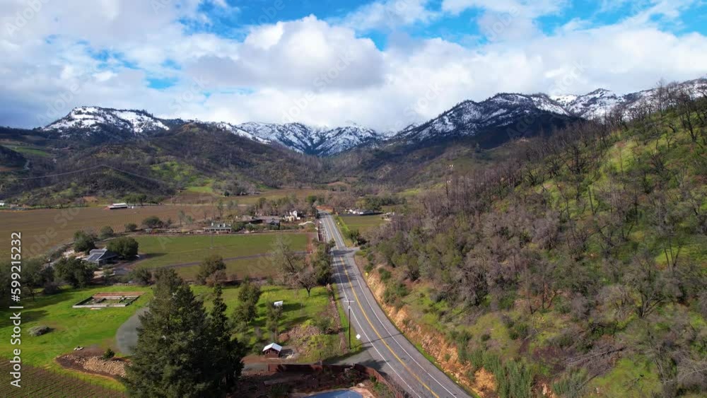 Fast aerial glide above Napa Valley vineyards following a road to snow white mountains Fast aerial glide above Napa Valley vineyards following a road to snow white mountains
