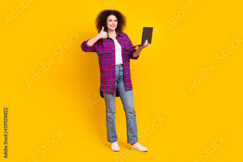 Full length photo of shiny confident woman dressed plaid shirt working modern device thumb up isolated yellow color background