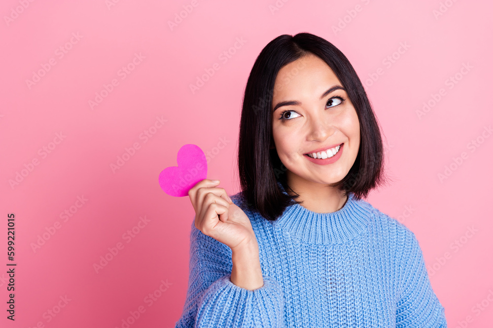 Portrait of gorgeous toothy beaming girl bob hairstyle blue sweater hold paper heart look empty space isolated on pink color background Portrait of gorgeous toothy beaming girl bob hairstyle blue sweater hold paper heart look empty space isolated on pink color background