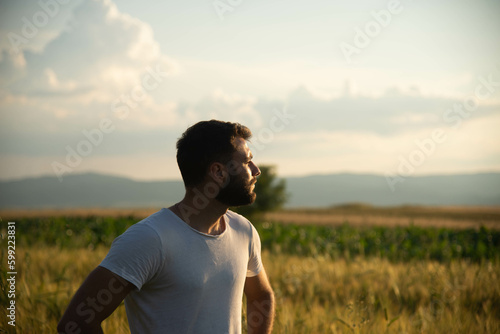 Happy young handsome man spending time in nature during the golden hour. Enjoying in sunset and looking to the sun. Walking through countryside. © Santijago