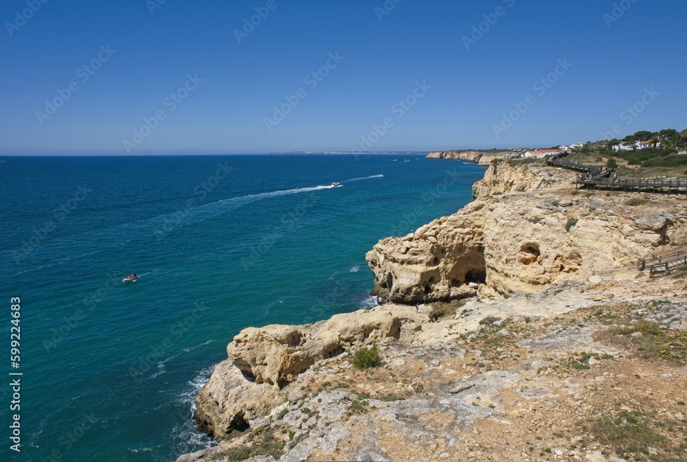 Carvoeiro, Portugal - April 11, 2023: Wonderful landscapes in Portugal. Scenic and coloured view of Carvoeiro coast in the Algarve region. Yellow rocky skerries. Sunny spring day. Selective focus Carvoeiro, Portugal - April 11, 2023: Wonderful landscapes in Portugal. Scenic and coloured view of Carvoeiro coast in the Algarve region. Yellow rocky skerries. Sunny spring day. Selective focus