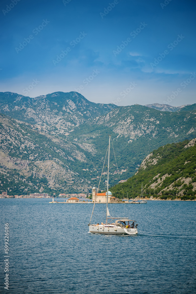 View of a floating white yacht towards Our Lady of the Rocks in the Bay of Kotor