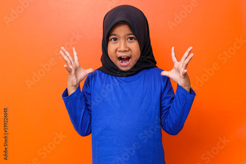 Asian muslim girl wearing hijab screaming against orange background.  photo