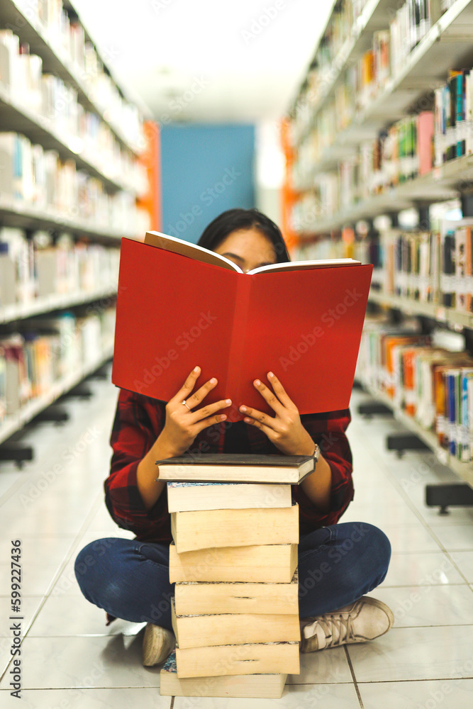 Young school girl sit on the floor covering face by the red book with