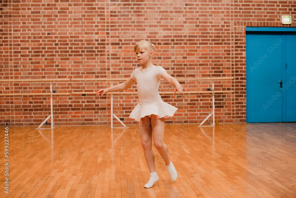 Cute charming ballerina little girl in ballet clothes is engaged in ballet dancing. Concept of happy childhood, children's hobbies.