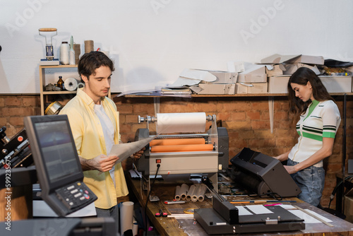 good looking typographer looking at printed paper near pretty colleague. photo