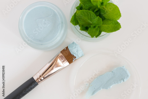 Glass jar with natural facial mask and leaf mint on glas plate and a brush for application on white background, close up. Selective fokus
