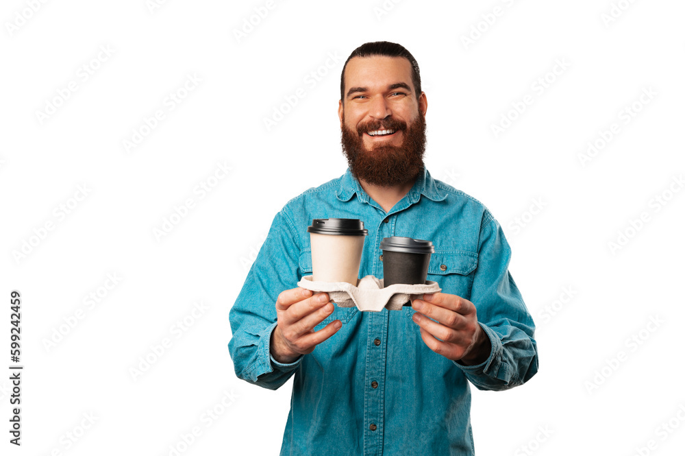 Friendly bearded man holding two cups of coffee to go is handing to the camera over white background. Friendly bearded man holding two cups of coffee to go is handing to the camera over white background.