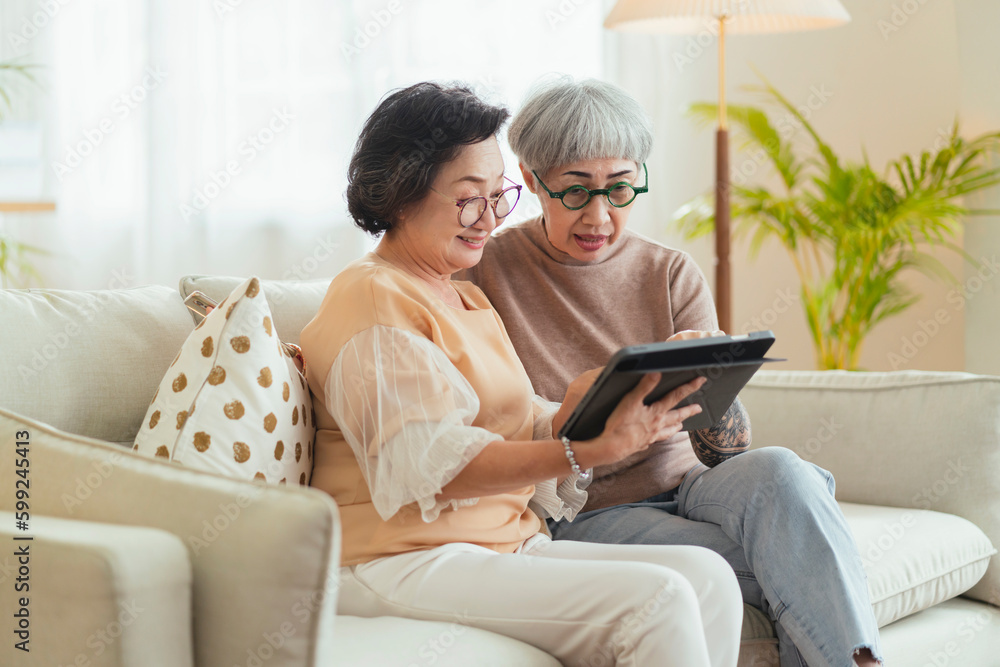 senior old asian aunt retired woman friend looking to old photo memory of herself together with good old time on sofa at home, retired asian woman spending their time together with tablet at home senior old asian aunt retired woman friend looking to old photo memory of herself together with good old time on sofa at home, retired asian woman spending their time together with tablet at home