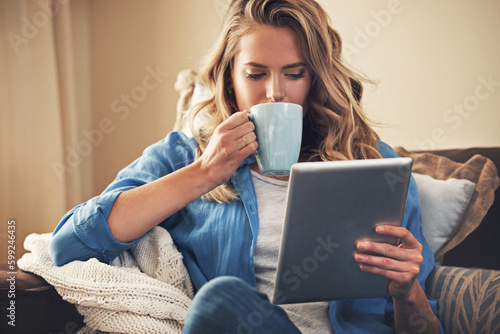 Theres something to interest everyone online. a relaxed young woman having coffee and using a digital tablet on the sofa at home.