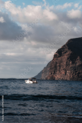 A boat sailing on the sea at sunset with cliffs in the background.
