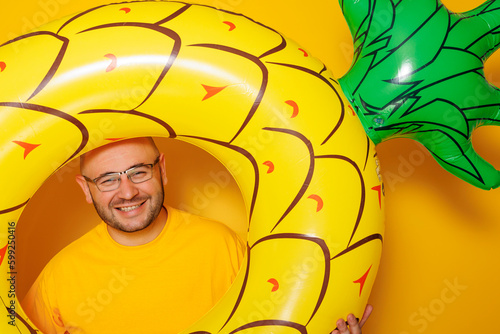 Man holding inflatable pineapple swim ring on yellow colored background
