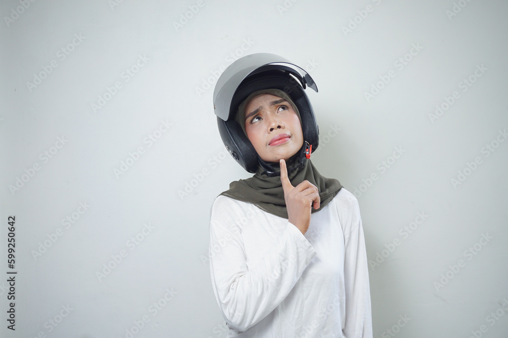Young asian muslim woman smiling and thinking using motorcycle helmet isolated on white background Young asian muslim woman smiling and thinking using motorcycle helmet isolated on white background
