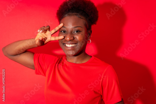 Young african american woman isolated on a red background smiling with the victory gesture, studio shoot