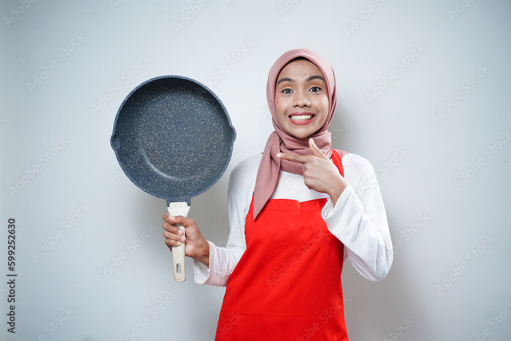 Young Asian woman housewife wearing kitchen apron cooking and holding pan isolated on white background Young Asian woman housewife wearing kitchen apron cooking and holding pan isolated on white background