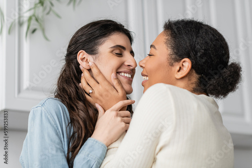 overjoyed multiracial woman with engagement ring on finger hugging with smiling girlfriend.