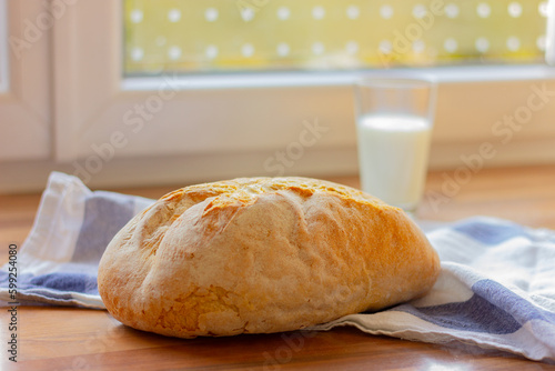 whole loaf of white bread and glass of milk on kitchen towel on a wooden table