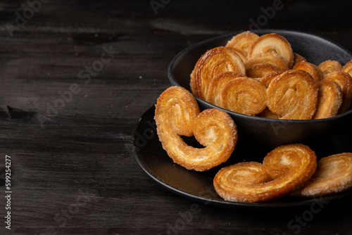 Top view of puff pastries in black bowl on dark table, selective focus, horizontal, with copy space