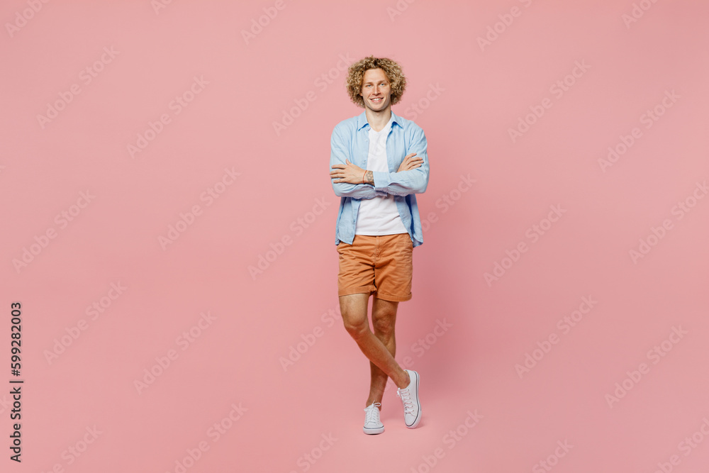 Full body smiling happy cheerful young blond man wear blue shirt white t-shirt hold hands crossed folded look camera isolated on plain pastel light pink background studio portrait. Lifestyle concept. Full body smiling happy cheerful young blond man wear blue shirt white t-shirt hold hands crossed folded look camera isolated on plain pastel light pink background studio portrait. Lifestyle concept.