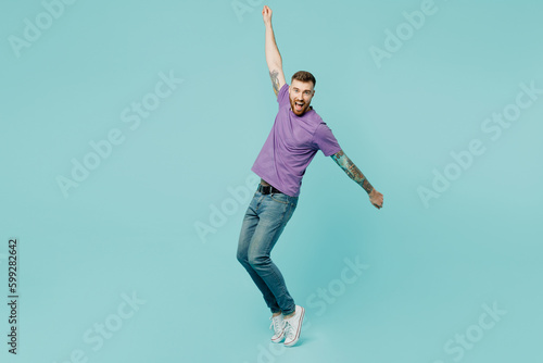 Foto Full body european young man he wears purple t-shirt stand on toes with outstretched hands leaning back dancing isolated on plain pastel light blue cyan background studio portrait