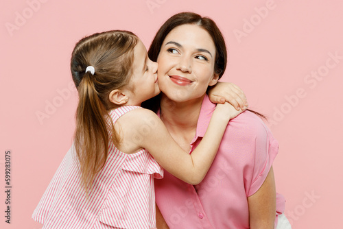 Happy fun adorable lovely woman wearing casual clothes with child kid girl 6-7 years old. Daughter kissing mother cheek  look aside isolated on plain pastel pink background. Family parent day concept.