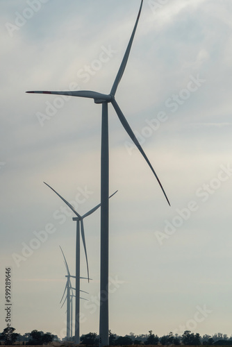 Row of windmills with rotating blades generate energy as renewable source for economy. Producing of alternative form of energy under clouds
