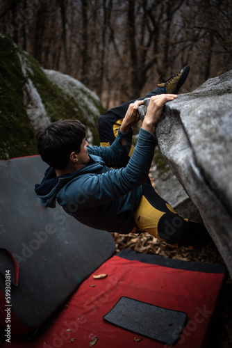 A rock climber climbing on a boulder rock outdoors. Group of friends involved in sports outside.