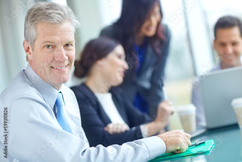 Pleased with the firms performance. A mature businessman sitting at a conference table with his colleagues in the background.